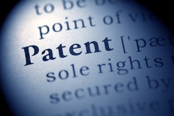 A hand holding a magnifying glass over a complex legal document filled with technical drawings and dense text.