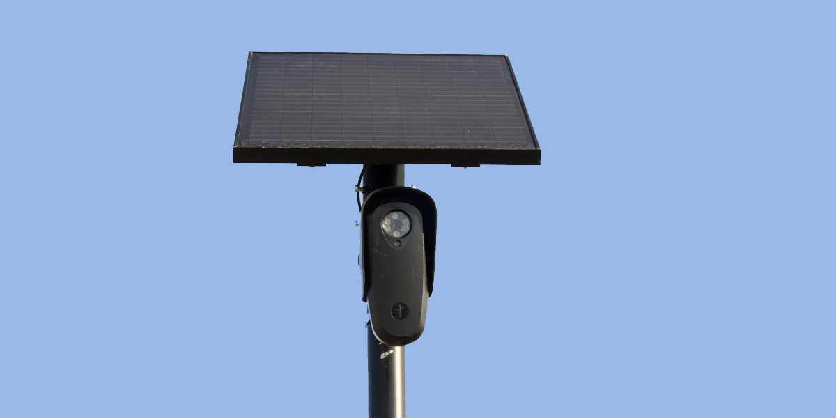 A close-up of a license plate reader camera mounted on a pole by a road.